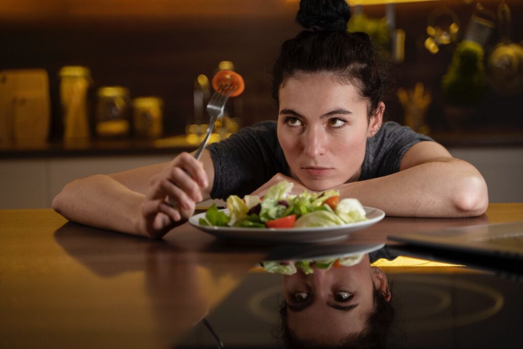 Femeie așezată la o masă în fața unei farfurii pline de salată